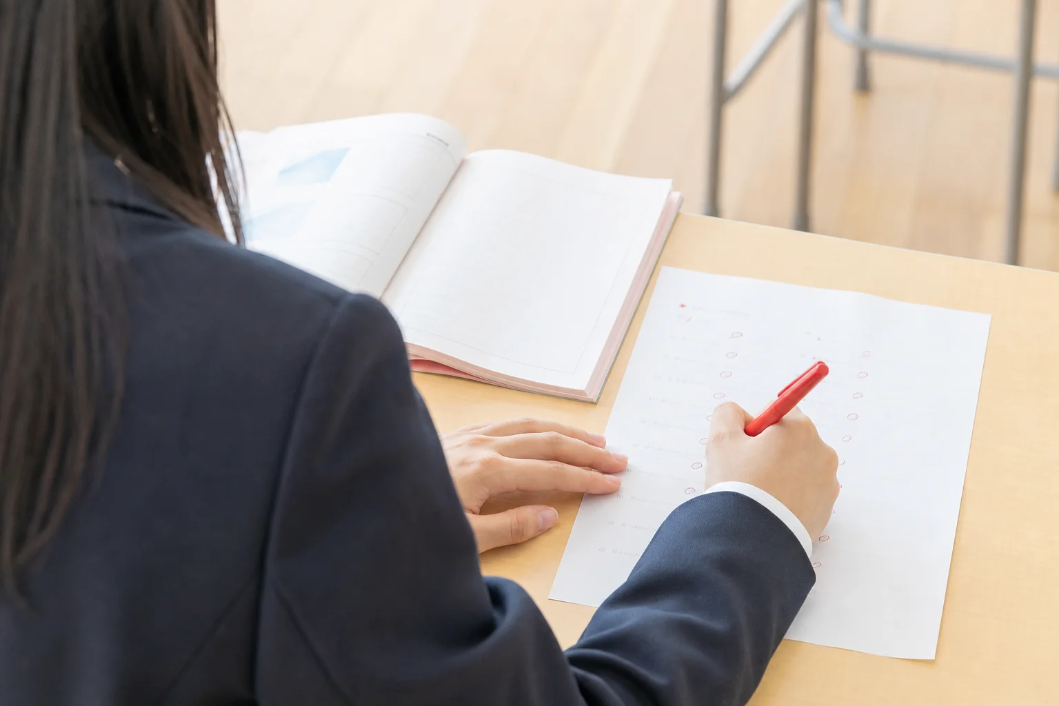 仕切りのない明るい教室の机で、予習してきたテキストをもとに小テストの答え合わせをしている手元