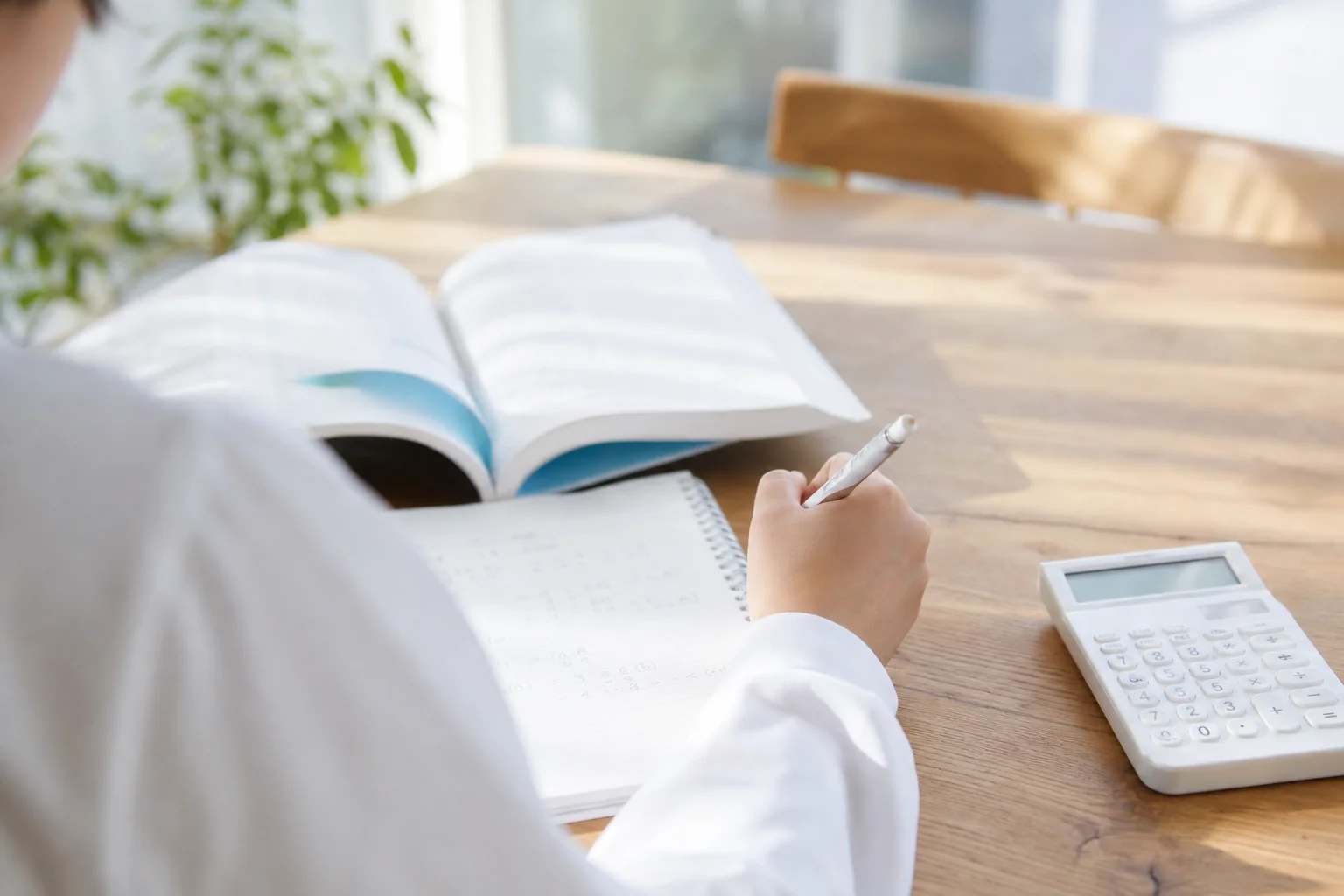 家のテーブルで電卓とノートを広げ、塾の月謝を書き出して計算している手元の様子